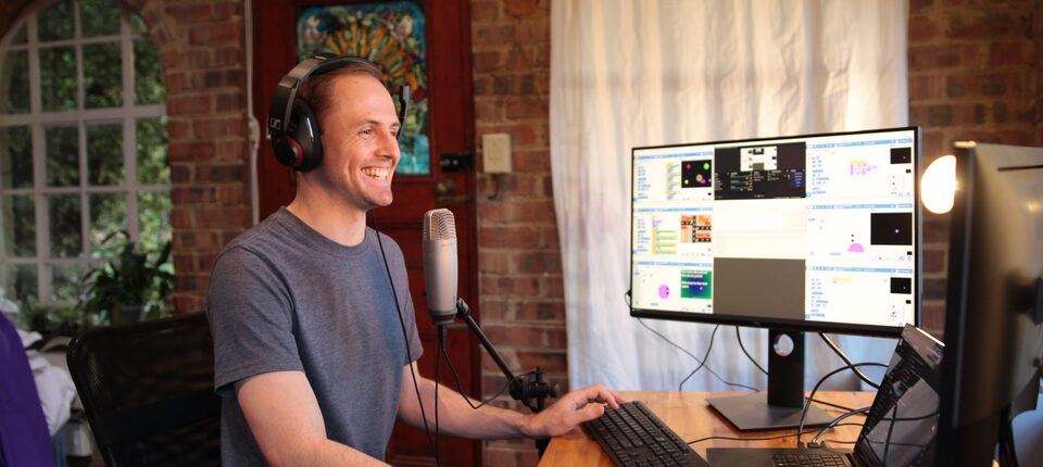 John Naiker teaching a live RocketHour class from home, headset on, block code on the screen beside him